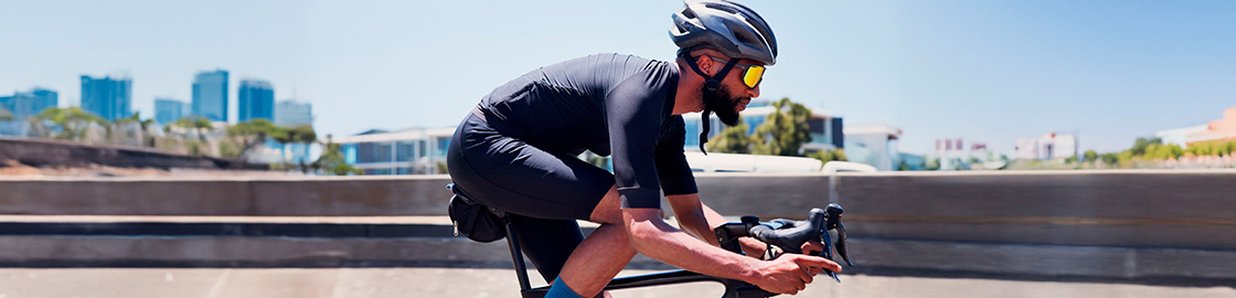 Foto de un ciclista con casco, lentes y ropa deportiva, rodando en la calle en medio de una competición